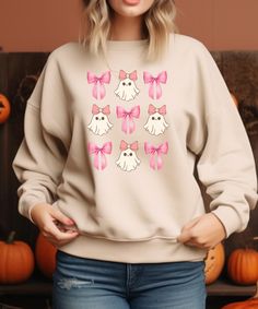 Elevate your autumn wardrobe with our adorable sweatshirt, featuring a charming design of pink bows and ghosts arranged in three stylish rows.  This cozy and trendy piece combines the sweetness of pastel pink with the festive spirit of fall, making it perfect for pumpkin patch outings, casual gatherings, or cozy days at home.  The playful design makes it a must-have for anyone who loves to embrace the season with a touch of whimsy. Comfortable, cute, and oh-so-fall--this sweatshirt is your new go-to for effortless autumn style! Fall Cotton Kawaii Sweatshirt, Customizable Pink Fall Sweatshirt, Fall Kawaii Graphic Print Sweatshirt, Embroidered Bow Sweatshirt, Pink Long Sleeve Halloween Sweatshirt, Autumn Wardrobe, Pink Bows, Sweatshirt Halloween, Autumn Style