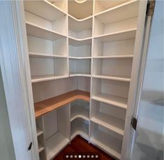 an empty white pantry with wooden shelves and wood flooring in the corner is shown