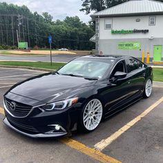 a black car parked in front of a building with white rims on it's tires