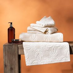 towels, soap and lotion are stacked on top of a wooden table in front of an orange background