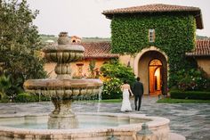 a bride and groom standing in front of a fountain