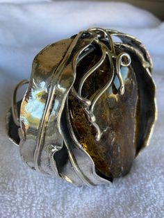 "227 gram Brutalist Style Vintage Amber Sterling Silver Cuff made in Poland. Made in Poland, this cuff is around 3 3/4\" long x 4\" wide x 1\" wide including silver work. The stone itself is around 3 1/4\" long x 2 1/4\" wide x 3/4\" thick. The wrist size is a little difficult to determine without a wrist mantle because of the way it's made, but it appears to be around a wrist size 8\"(7\" end to end plus an inch gap). I can take it to my jeweler to confirm the size. When you hold it to the ligh Unique Bronze Cuff Bracelet For Formal Occasions, Handmade Bronze Cuff Bracelet For Formal Occasions, Unique Polished Cuff Bracelet As Gift, Unique Polished Cuff Bracelet Gift, Unique Hand Forged Cuff Bracelet For Formal Events, Unique Polished Cuff Bracelet For Gift, Unique Hand Forged Cuff Bracelet For Formal Occasions, Unique Cuff Bracelet For Anniversary, Unique Bangle Cuff Bracelet For Anniversary