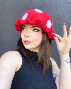 a woman wearing a red knitted mushroom hat with white polka dots on her face