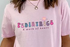 🌟 Description: Celebrate the heart and soul of pediatric nursing with our adorable shirt that proudly displays the phrase "Pediatrics: A Work of Heart." Designed with pediatric nurses in mind, this shirt combines comfort, style, and a touch of colorful charm, making it a perfect addition to any nurse's wardrobe. Crafted from the high-quality Comfort Colors 1717 material, it offers a soft, durable, and vibrant wear that is perfect for those who bring care and joy to little patients every day. 🌈 Pediatric Nurse, Pediatric Nursing, Charm Making, Nurse Shirt, Heart And Soul, Nursing Shirts, Comfort Style, Pediatrics, Heart Design