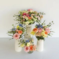 three white vases filled with different colored flowers