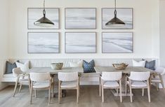 a dining room table with chairs and pictures on the wall above it, along with white benches