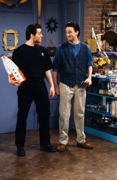 two men standing next to each other in front of a blue shelf filled with items