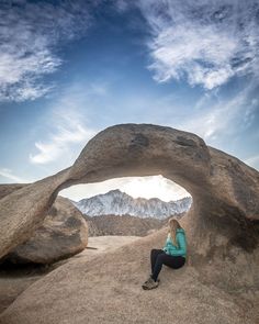 a woman sitting on top of a large rock in the middle of a desert area