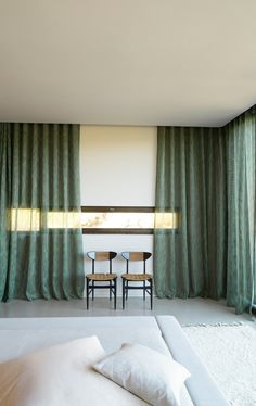 two chairs are sitting in front of a window with green drapes on the windowsill