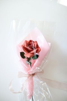 a pink rose wrapped in plastic on a white surface with a ribbon around the edge