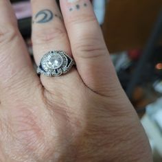 a woman's hand with a diamond ring on her left finger and tattoos on the right