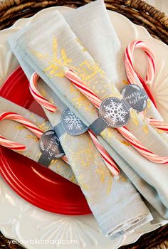 candy canes are wrapped in napkins on a red and white plate with silverware