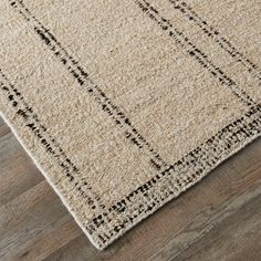 a beige rug with black lines on the top and bottom, sitting on a wooden floor