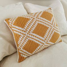 an orange and white knitted pillow sitting on top of a bed next to pillows