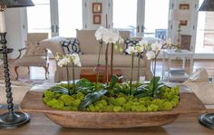 a wooden bowl filled with white flowers on top of a table next to two lamps