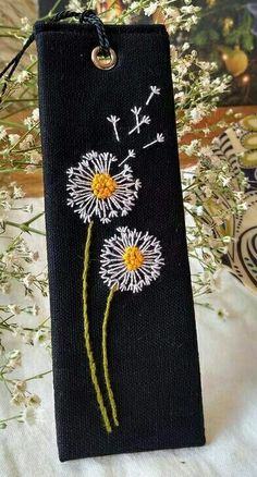 a black book with white and yellow dandelions painted on the cover, sitting next to some flowers