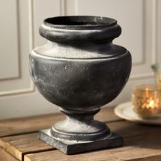 a large metal vase sitting on top of a wooden table next to a candle holder