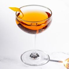 a glass filled with liquid sitting on top of a white counter next to an orange peel