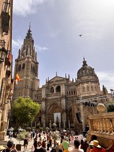 many people are walking around in front of an old building with towers and spires