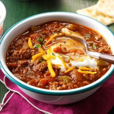 a bowl of chili and cheese soup with a spoon in it on a purple napkin