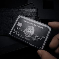 an american express credit card being held in front of a black leather wallet, which is open