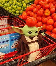 a baby yoda doll sitting in a shopping cart next to tomatoes and other produce