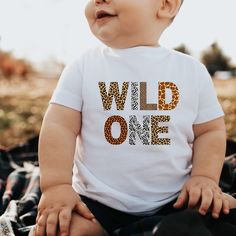 a baby wearing a white shirt with the word wild one printed on it's chest