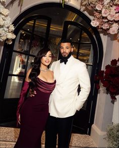 a man and woman standing next to each other in front of a doorway with flowers