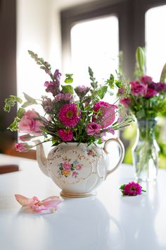 pink flowers are in a teapot on a table next to two vases filled with water