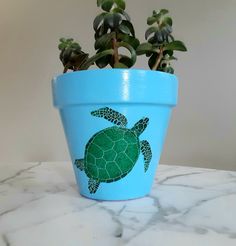 a potted plant with a green turtle painted on it's side sitting on a marble table