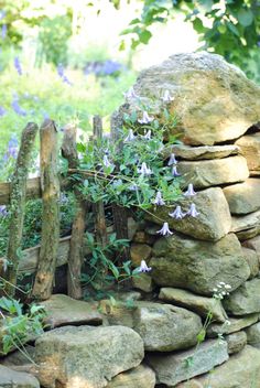 a stone wall with flowers growing out of it and some wooden fence posts in the background