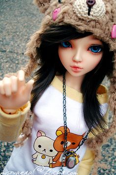 a doll is wearing a bear hat and holding her hand up to the camera while standing in front of a building