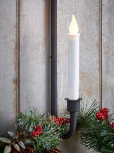 a white candle is lit in front of some christmas wreaths and pine cones on the wall