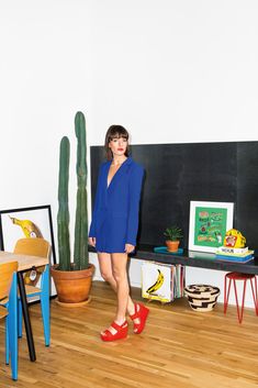 a woman standing in front of a blackboard wearing red shoes and a blue blazer