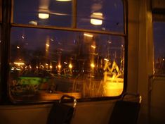 an empty seat in front of a window with the night time lights on behind it