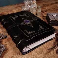 an old black book sitting on top of a wooden table next to bottles and other items