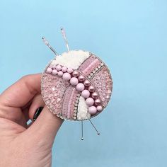 a hand holding a pink and white brooch with beading on it's side