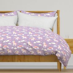 a bed with purple unicorns and rainbows on the comforter is in front of a white wall