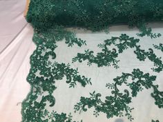 green lace with flowers and leaves on white fabric, laying on top of a table