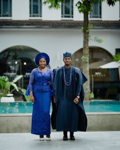 a man and woman standing next to each other in front of a building with a pool