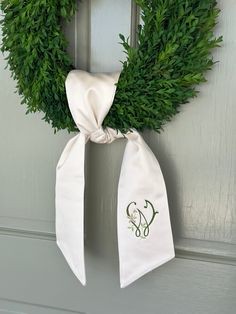 a green wreath hanging on the front door with a monogrammed bow tied around it