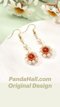 a pair of red and white earrings sitting on top of a table next to flowers