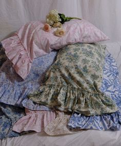 a pile of different colored pillows on top of a white sheeted bed covered in pink and blue sheets