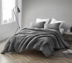 a bed in a room with white walls and wooden flooring, along with a gray comforter