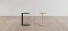 two small tables sitting on top of a wooden floor next to each other in front of a white wall