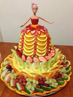 a cake made to look like a woman in a dress on top of fruit and vegetables