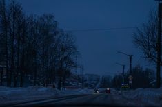 cars driving down the road at night in winter time with snow on the ground and bare trees