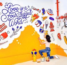 a woman sitting on the floor painting a wall with colorful stickers and words above her