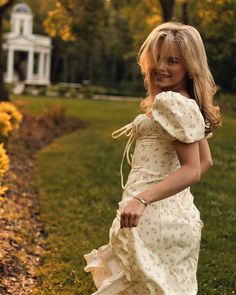 a woman in a white dress is walking through the grass with her hand on her hip