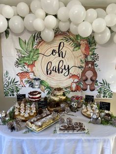 a table topped with lots of desserts and balloons in front of a sign that says oh baby